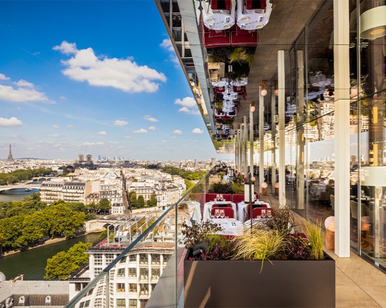 A beautiful outside balcony terrace with dining tables, overlooking a view of Paris including the Eiffel Tower