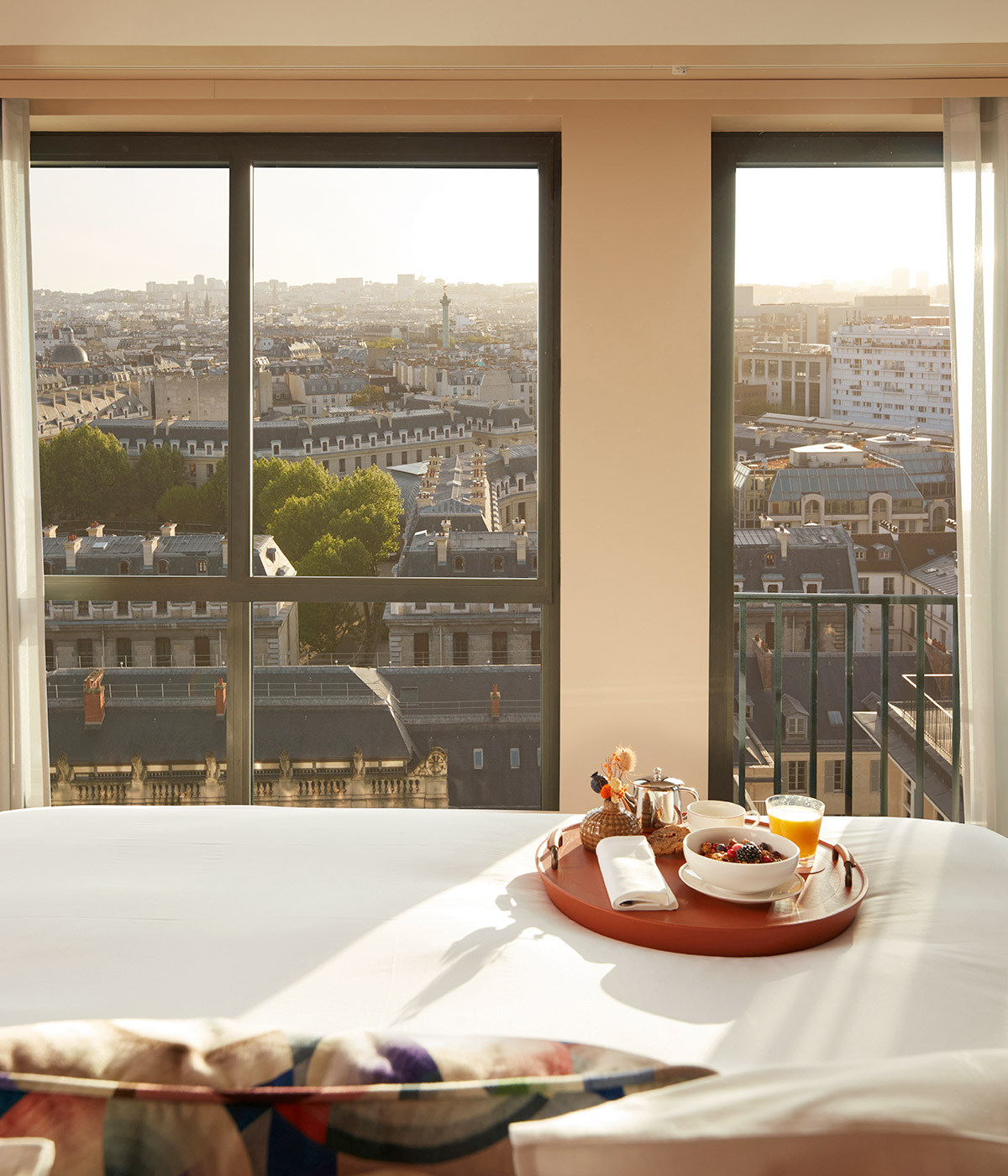 A bed with. a breakfast tray perched on the blanket looks out over a beautiful view of Paris.