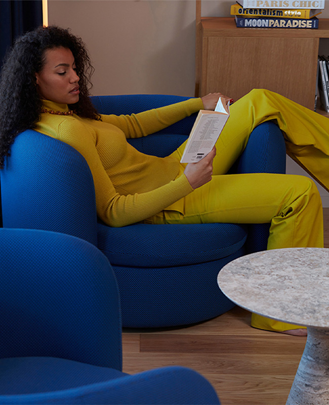 Woman laying in blue armchair reading in front of a marble coffee table