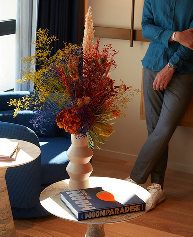 A man leaning on the wall in from of a blue armchair and two marble coffee tables