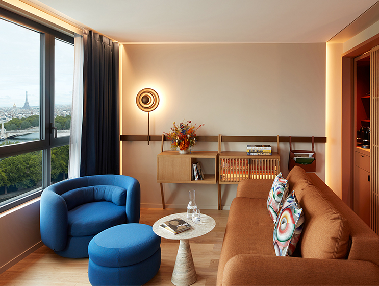 Spacious hotel room seating area with armchair, coffee table and couch overlooking Paris