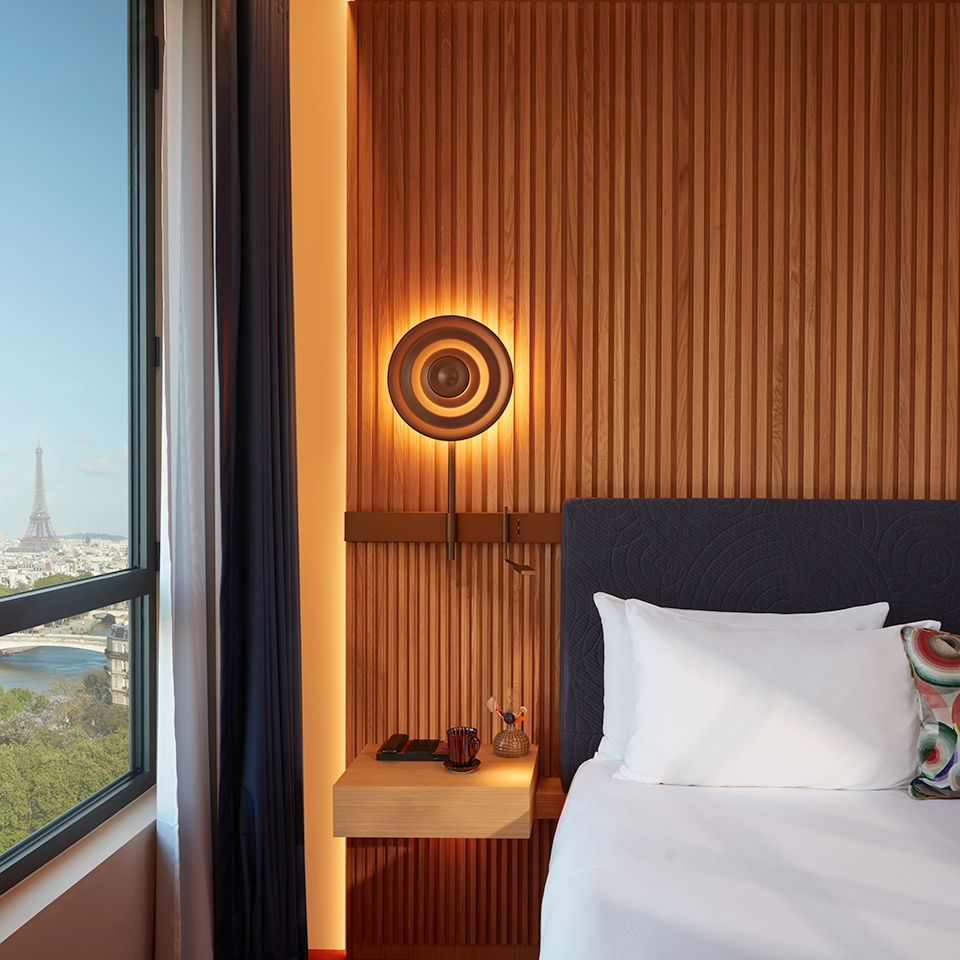 A view of the room including pillows, soft headboard, bedside lamp and view of the Eiffel tower.