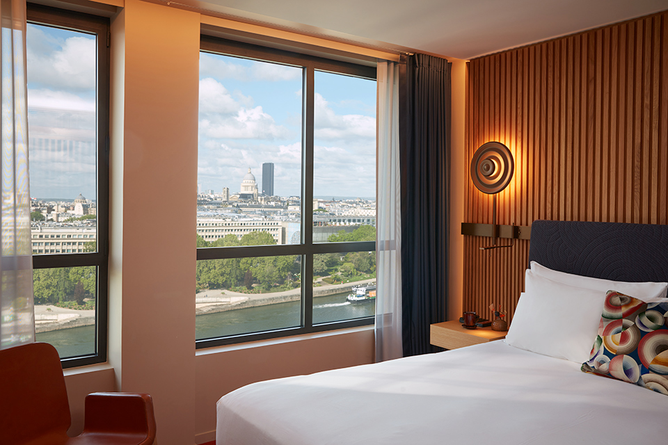 http://Corner%20view%20of%20the%20white%20sheets%20on%20the%20bed%20and%20the%20Paris%20skyline%20through%20the%20glass.