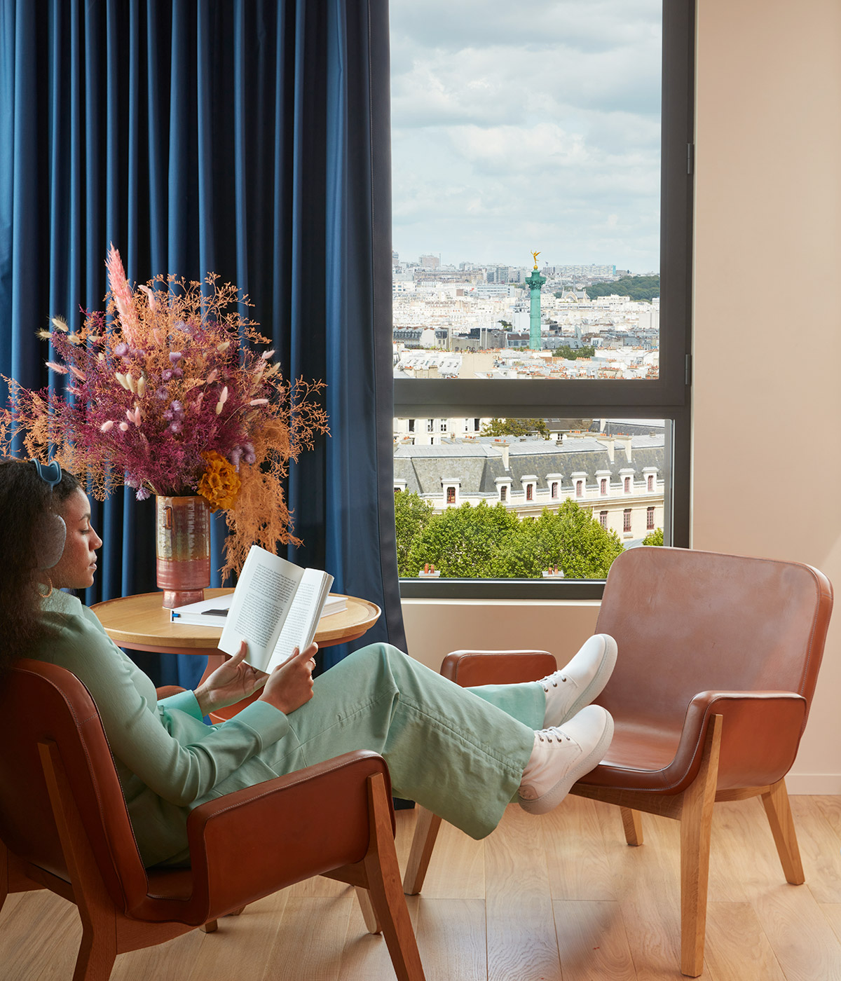 Lady in green reads a book with a view of Paris just through the window.