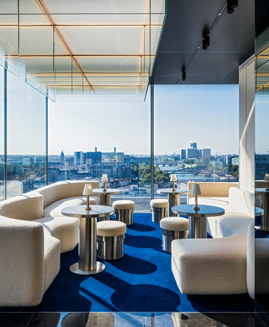 Natural light fills a seating area from the full-length windows surrounding the bar, with a beautiful view of Paris