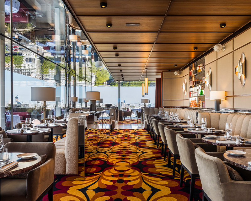 The inside of a stylish restaurant with full length windows.