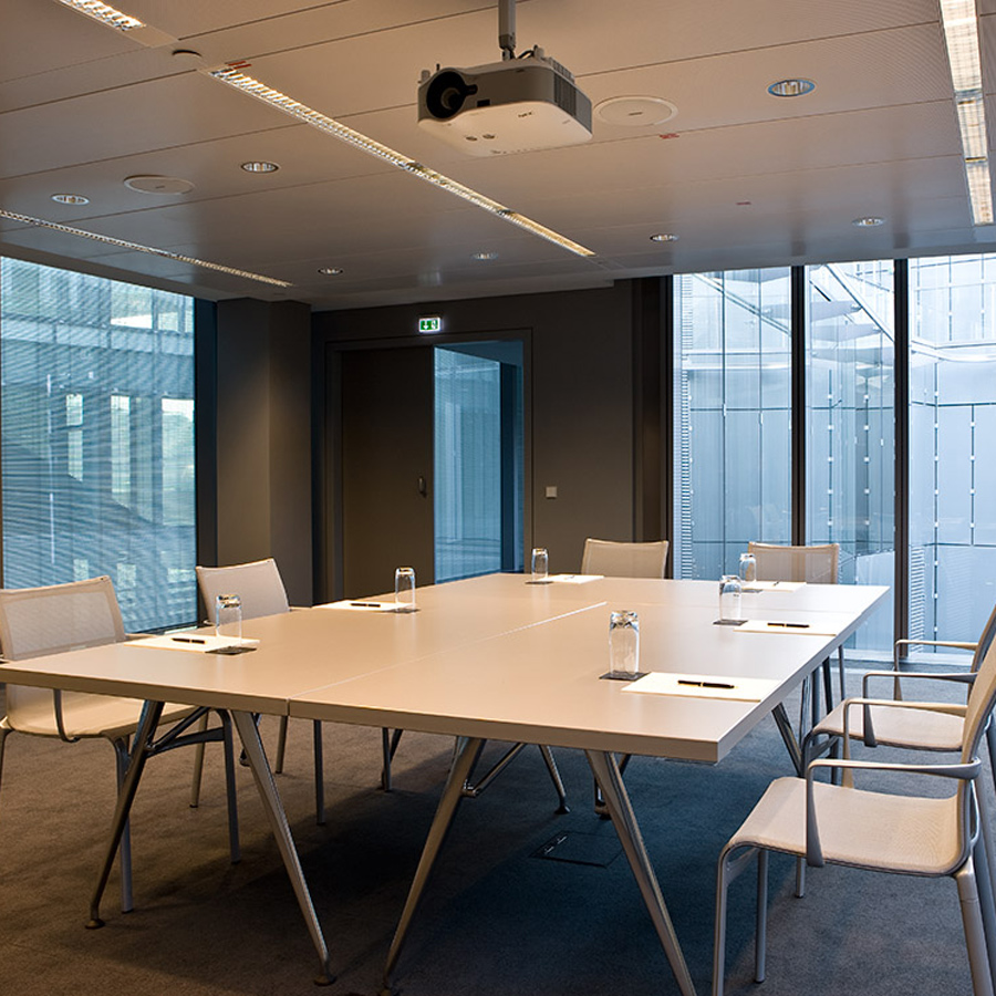 Meeting room with large white table and 6 chairs around it, with a projector above