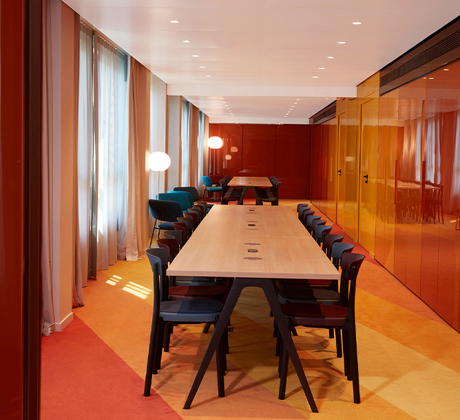 A long, autumnal coloured room with two large meeting tables and chairs. 