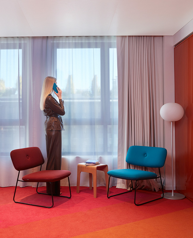 Woman on the phone standing in front of a window next to two chairs