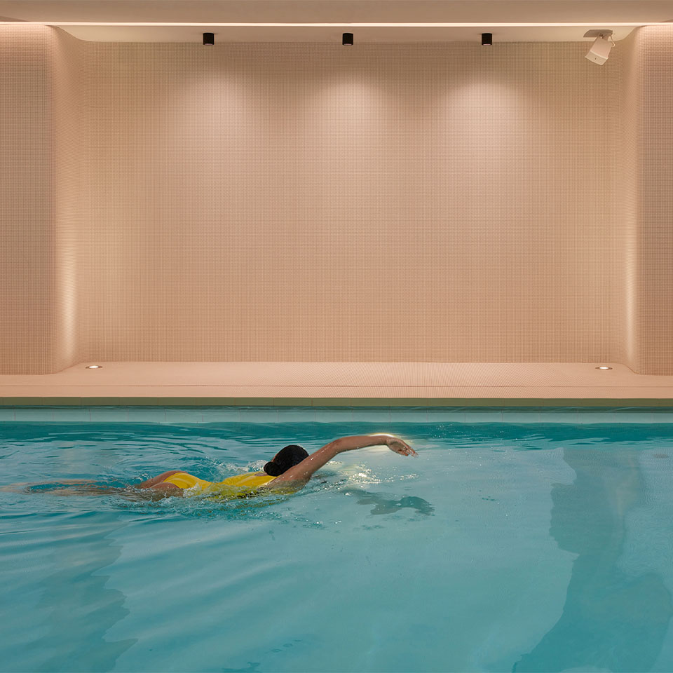 A women in a yellow swim suit swimming in an indoor pool