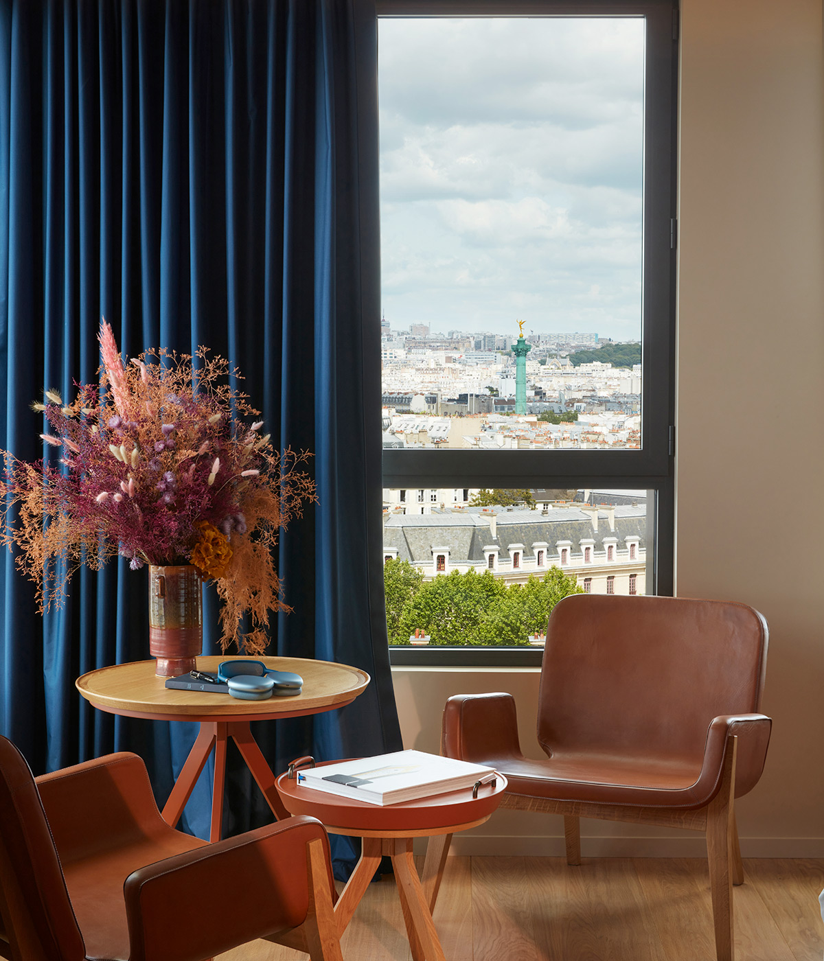Chairs and a table await a guest with flowers on the table and a sunny view of paris through the large window.