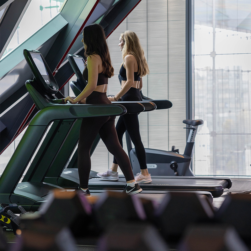 two people on their treadmills and a stack of black rubber dumbells