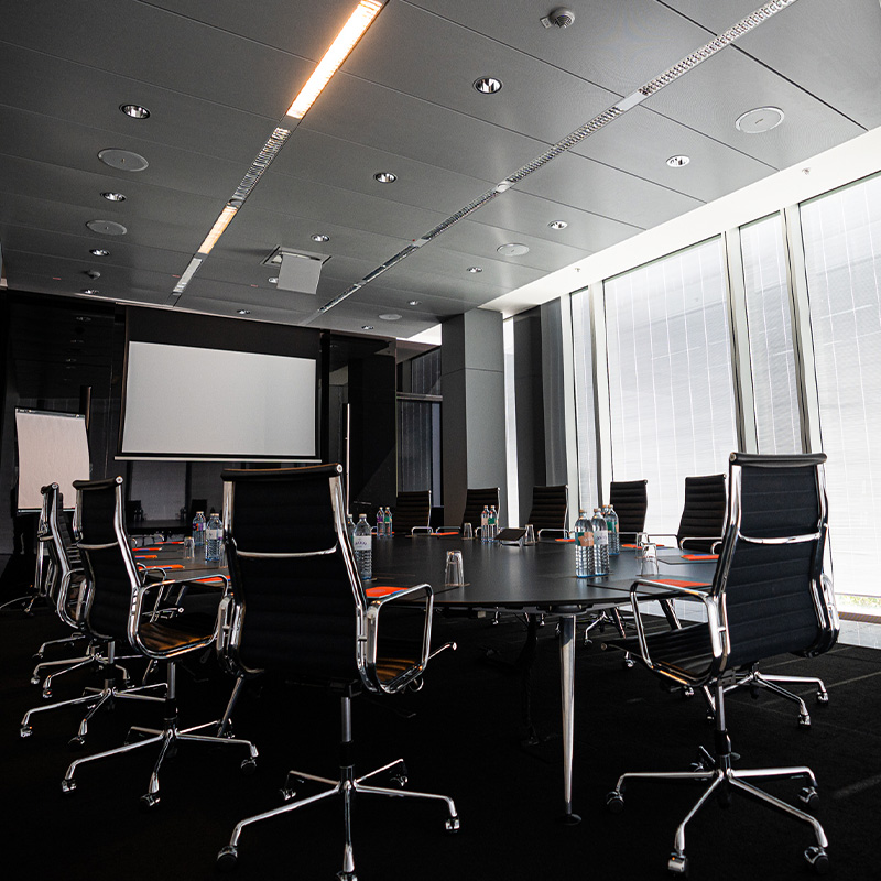A round meeting table next a large projector screen and full length window with a view of Vienna