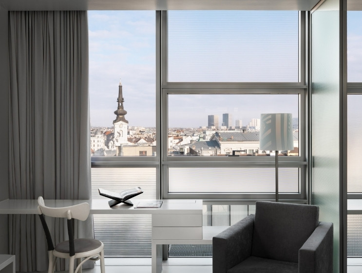 Modern office with sleek furniture, large windows showcasing a cityscape featuring a church spire and skyscrapers. Bright, airy, and minimalist ambiance.