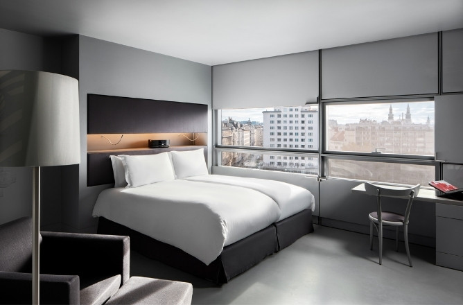 http://Modern%20hotel%20room%20with%20a%20large%20bed,%20crisp%20white%20linens,%20gray%20walls,%20and%20a%20city%20view%20through%20wide%20windows.%20Cozy%20armchair%20and%20sleek%20desk%20complete%20the%20scene.