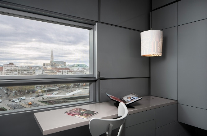 http://A%20sleek%20modern%20office%20with%20gray%20paneled%20walls%20and%20a%20large%20window%20revealing%20a%20city%20view%20with%20a%20church%20spire.%20A%20white%20chair%20faces%20a%20desk%20with%20magazines.