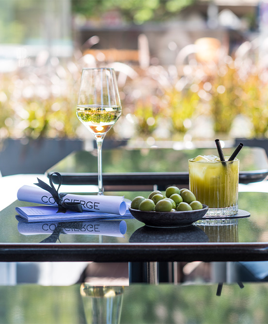 A glass of wine, olives, a cocktail and menu are placed on one of three tables in an outside area. 