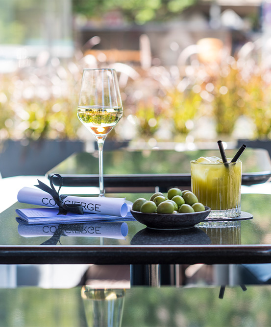 A glass of wine, olives, a cocktail and menu are placed on one of three tables in an outside area.