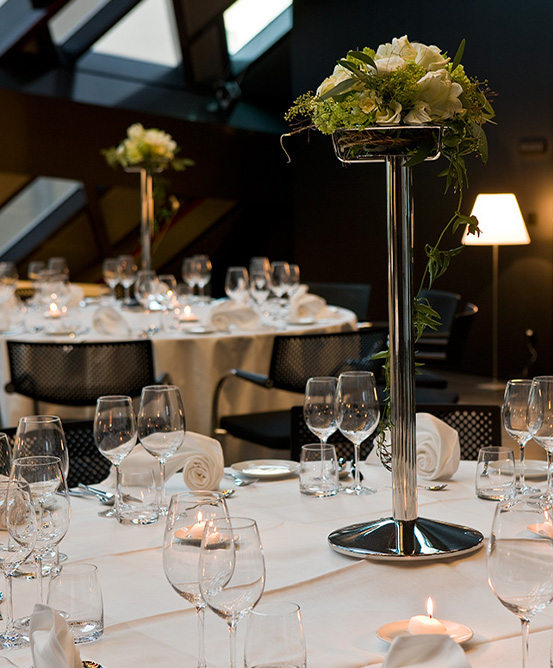 Round banquet tables forrmally set with tall silver flower vase