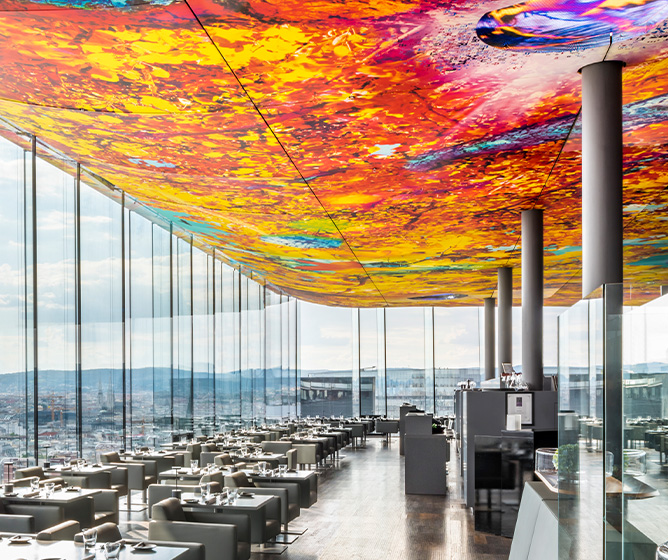 A large restaurant with surrounding windows and a large colourful mural on the ceiling. 