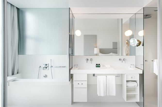 http://A%20white%20double%20sink%20vanity%20fitted%20with%20a%20large%20mirror,%20shelving%20units%20and%20make-up%20mirror%20next%20to%20a%20deep%20bathtub