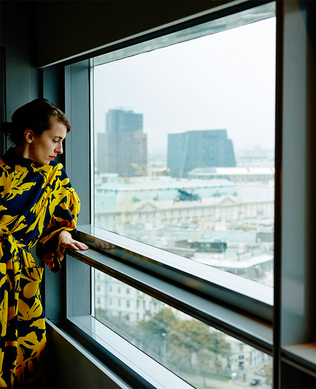 A women in a blue annd yellow dress looking out of a window with a view of the Viennese skyline
