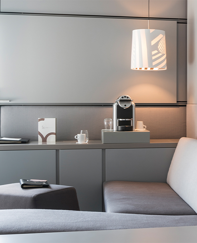 A table with Nespresso Coffee machine, glasses, white mugs and SO/ Vienna menu in front of a comfortable corner couch