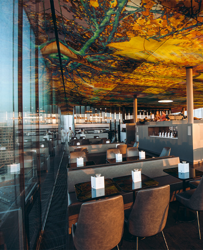 A large restaurant underneath a beautiful ceiling mural with full length windows overlooking the Viennese skyline