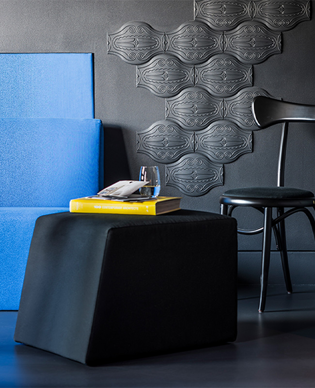 A black chair and footstool, with a book and drinking glass on top of it, placed next to a deep blue couch.