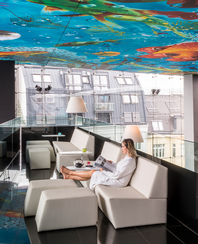 A woman sitting on a lounger below a colourful ceiling mural