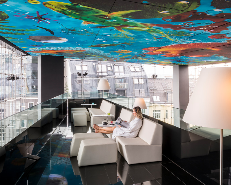 http://A%20woman%20sitting%20on%20a%20lounger%20below%20a%20colourful%20ceiling%20mural