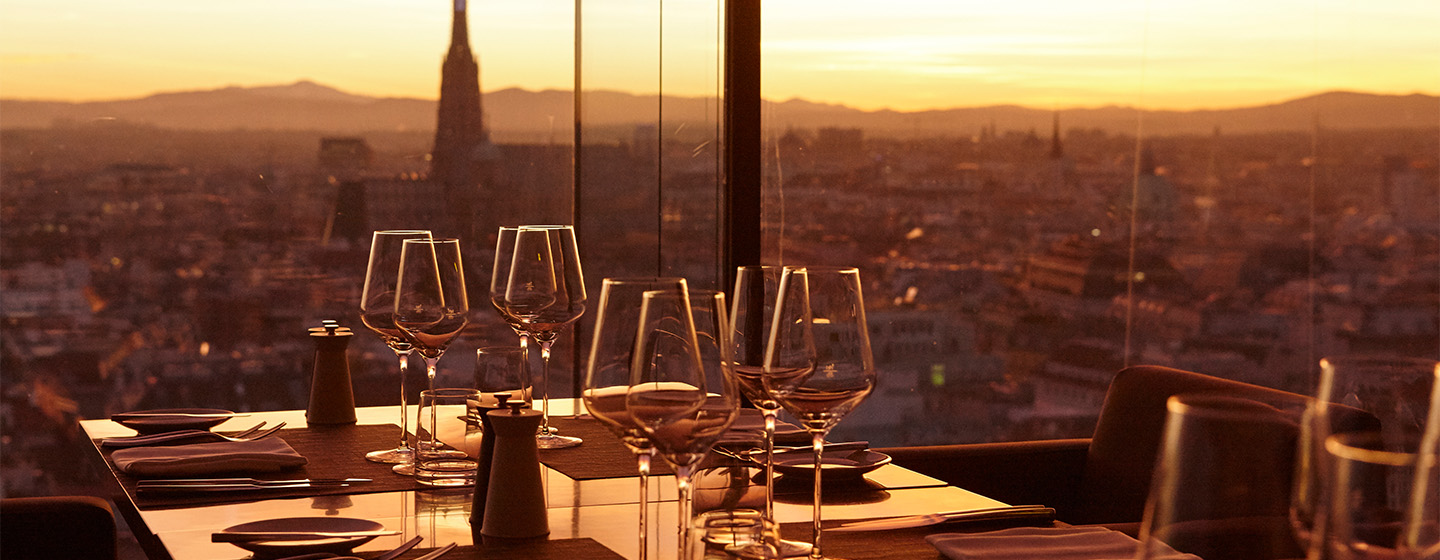 A beautiful sunset orange light shines through a full length window onto a formally set restaurant table