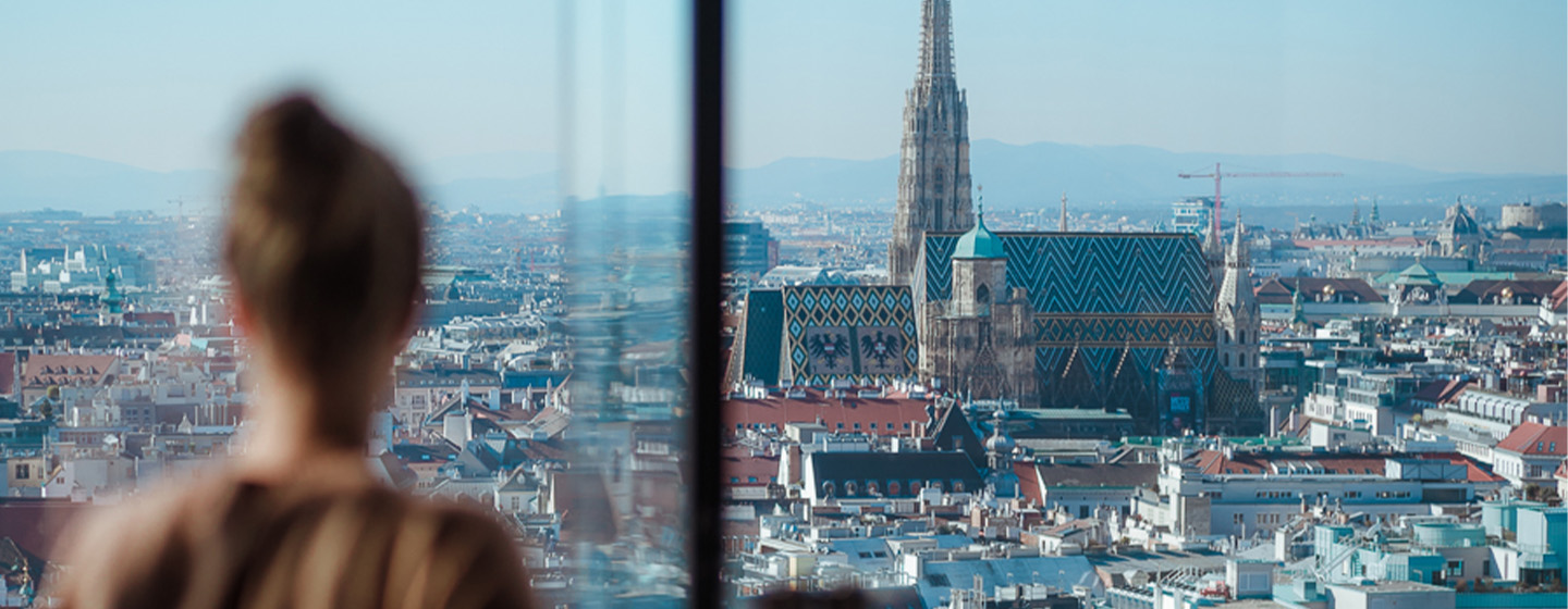 A women staring out of a full length window showing the breathtaking view of Vienna's skyline