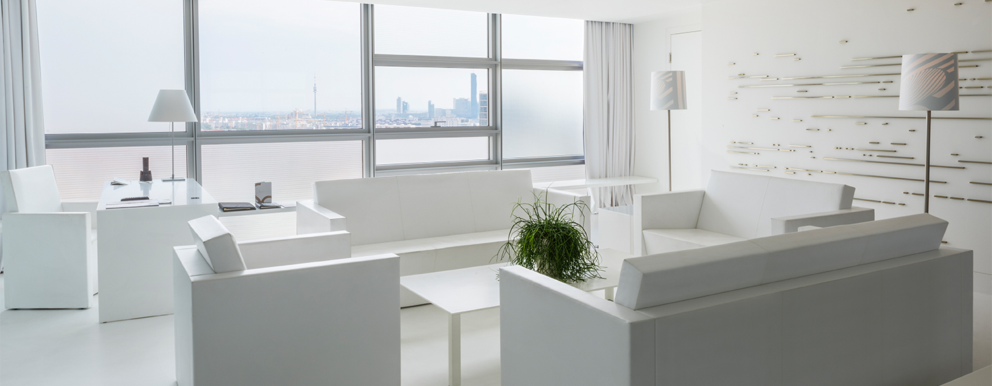 Natural light for a large window illuminating a large all-white room with two couches and armchairs and desk