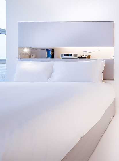 A pristine white hotel room with a double bed and an open sliding showing a white bathroom