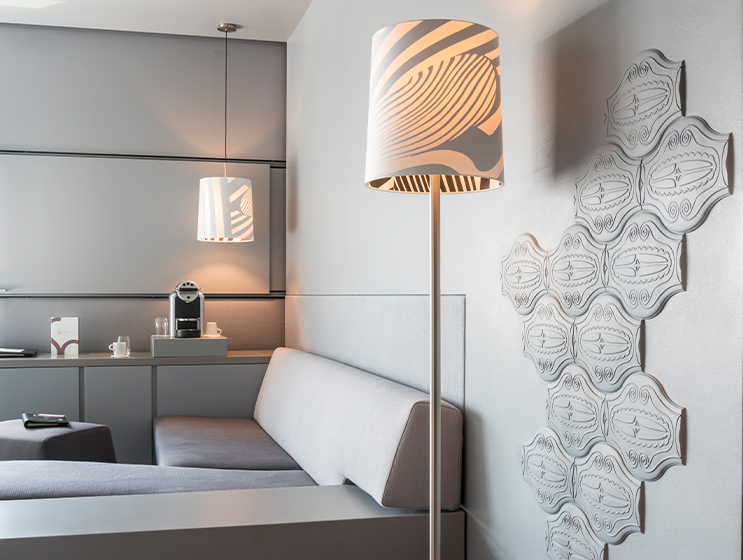 Wohnzimmer mit grauem Sofa, gemusterter Lampe und sechseckigen Wandbildern, die eine stilvolle, minimalistische Atmosphäre schaffen.