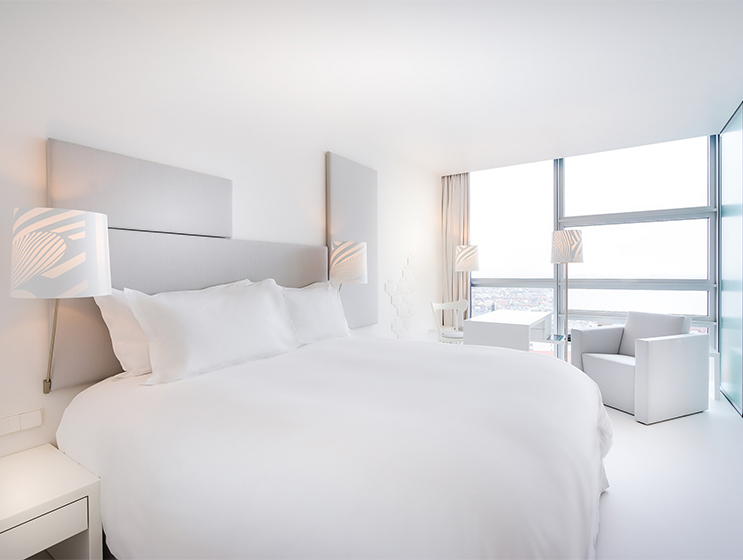 Modernes, helles Hotelzimmer mit einem Kingsize-Bett, eleganten Möbeln und großen Fenstern mit malerischer Aussicht.