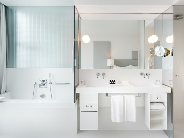 Ein weißer Doppelwaschtisch mit großem Spiegel, Regalen und Kosmetikspiegel neben einer tiefen Badewanne.
