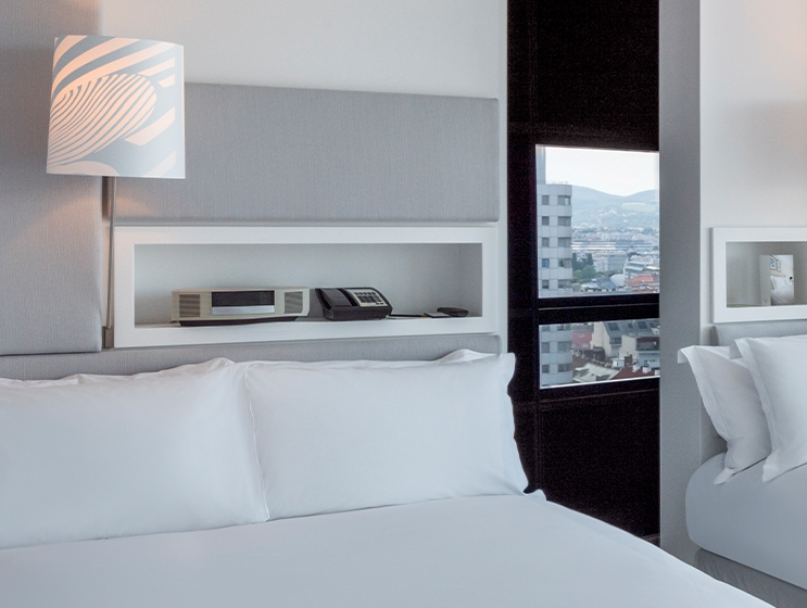 Modernes Hotelzimmer mit großem Bett mit weißer Bettwäsche, stilvoller Lampe und Blick durch große Fenster.