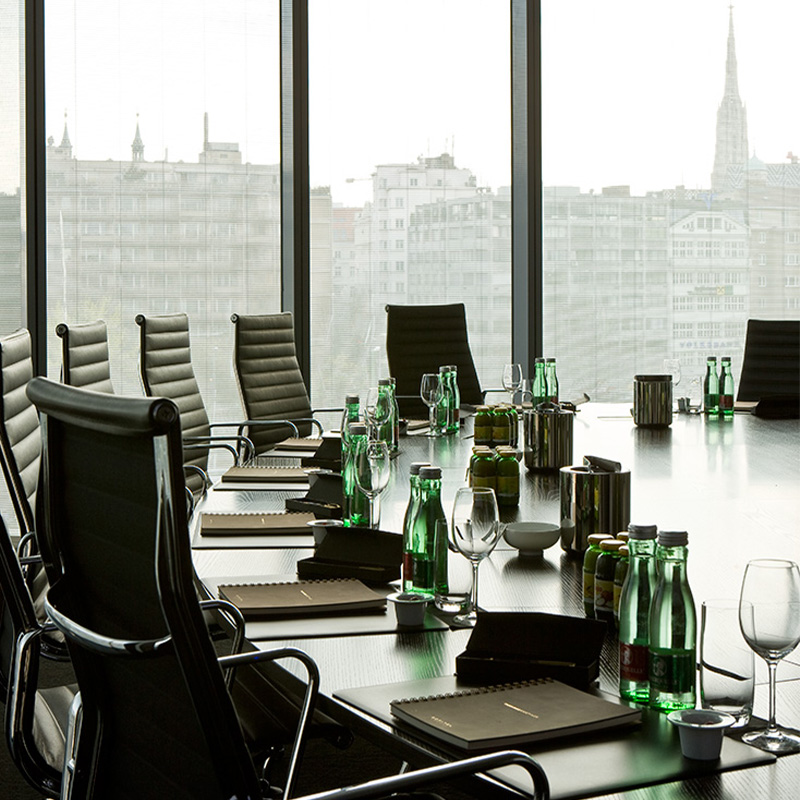 A round meeting table equipped with beverages and notepads next a full length window with a view of Vienna