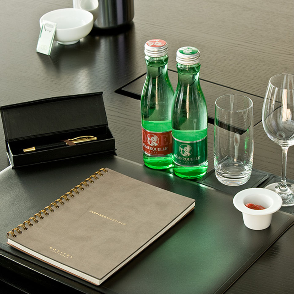 A note book and pen next to bottles of water and glasses. 