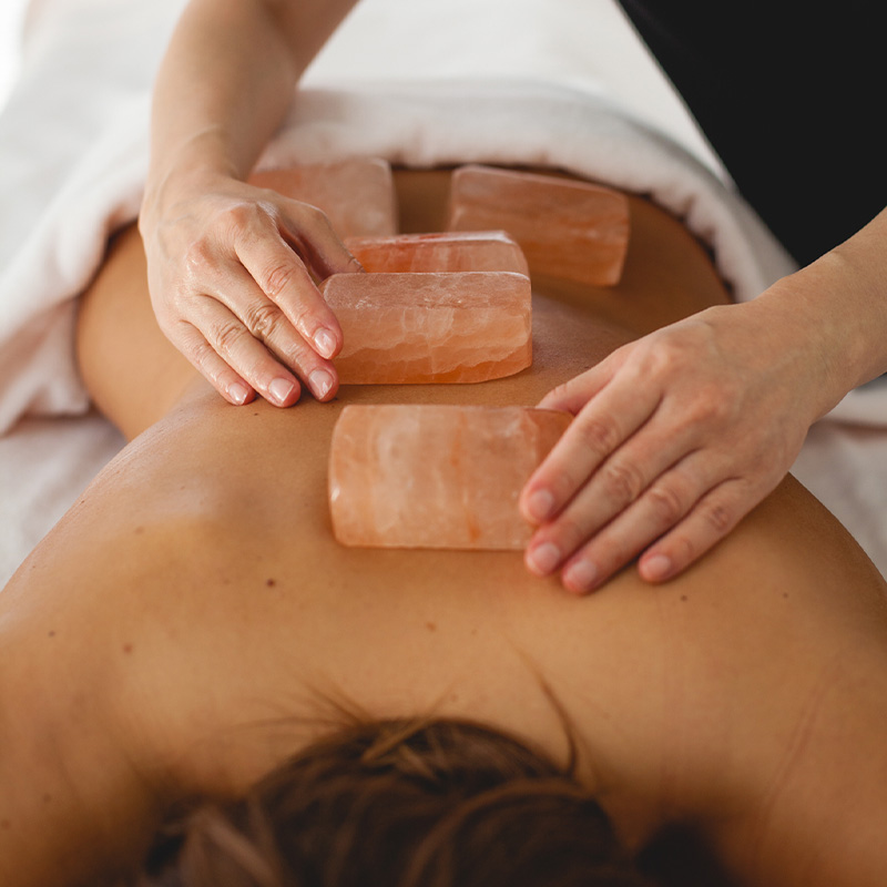 Hands placing cubed orange crystals on a woman's back