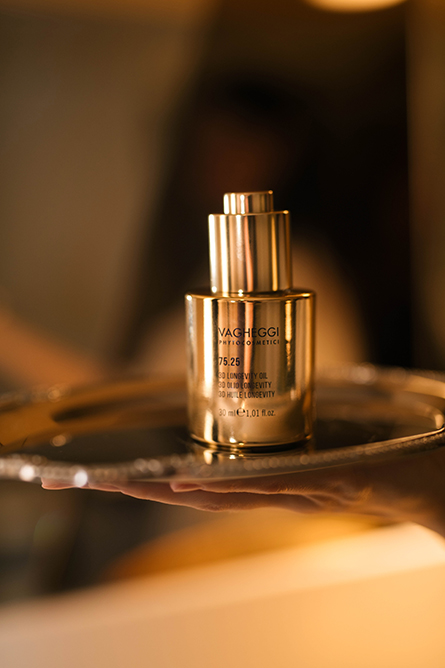 A gold bottle of Vagheggi serum on a reflective tray, held by a hand in warm lighting, conveying elegance and luxury skincare.