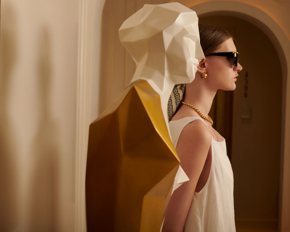 A woman standing in a hotel corridor, posing with a tactile mannequin placed for visually impaired guests. The corridor is well-lit, with modern interiors and a polished floor.”