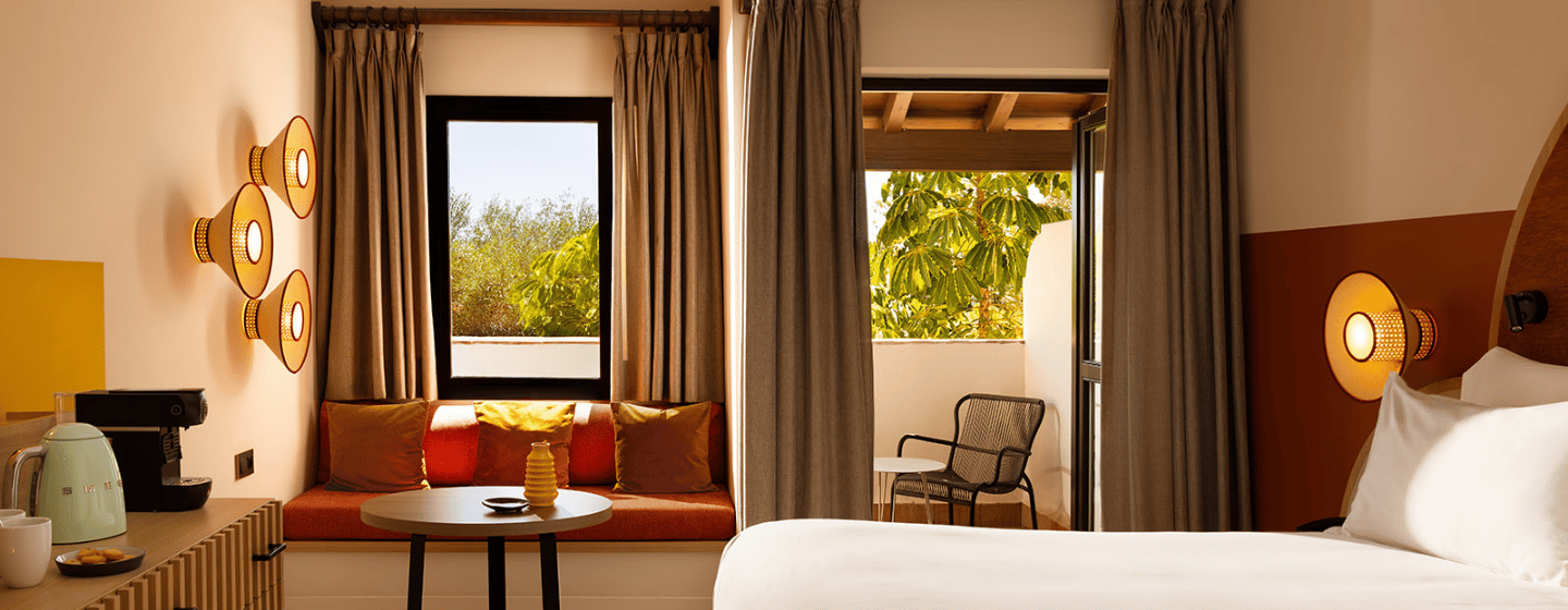 A hotel room featuring a neatly made bed, a large window allowing natural light, and a comfortable chair.