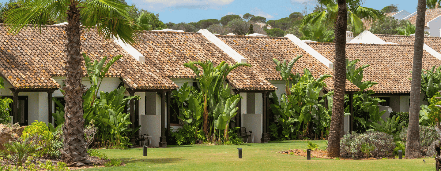 A row of charming cottages surrounded by palm trees and lush green grass, creating a serene tropical atmosphere.