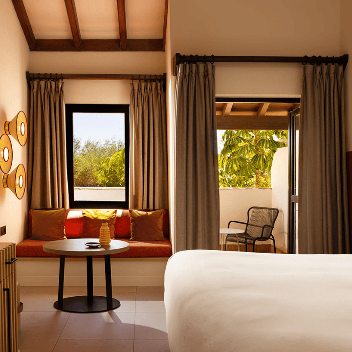 A hotel room featuring a neatly made bed, a large window allowing natural light, and a comfortable chair.