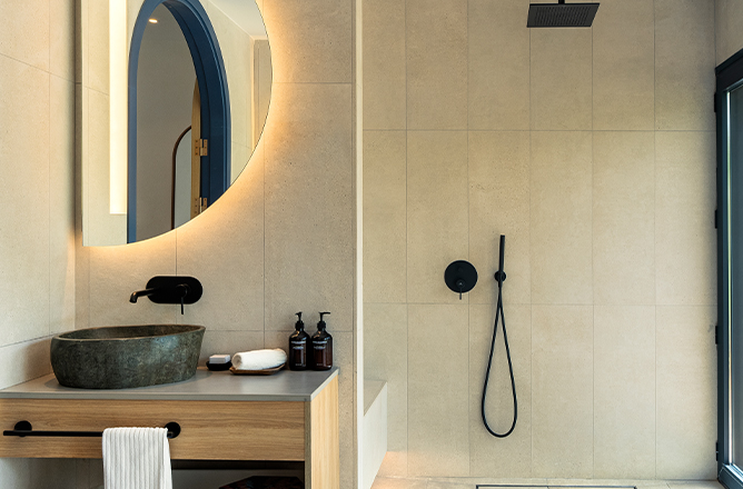Un cuarto de baño con un gran espejo redondo sobre el lavabo y una amplia zona de ducha.