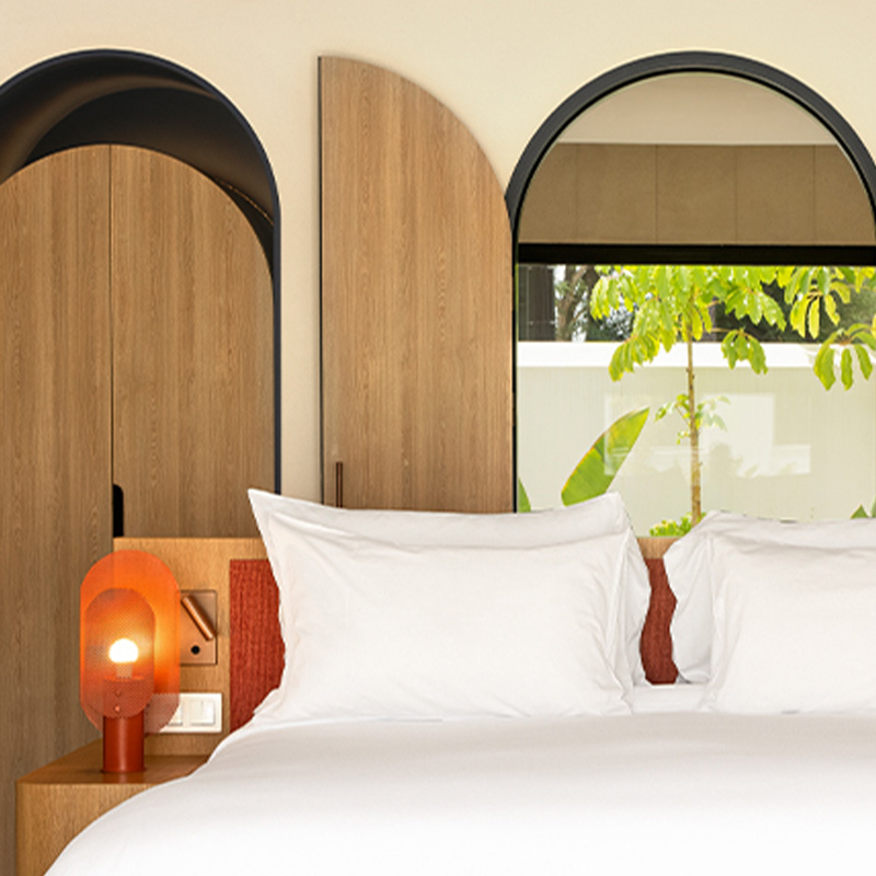 Vista de la cama king y mesa auxiliar con lámpara naranja.