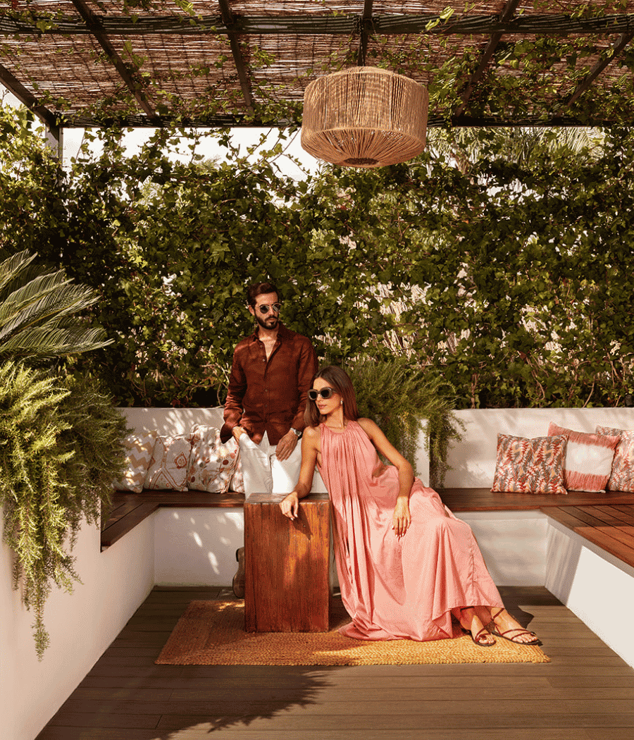 A man and woman sit on a wooden bench, surrounded by a lush wall of green plants.